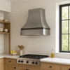 36 inch zinc range hood with recessed apron and bell shaped body in European style kitchen, smooth zinc canopy above classic cabinetry and stone surfaces