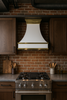 24 inch painted white metal range hood with brass detailing in Soho loft kitchen, glossy canopy above range with brick walls and industrial accents