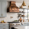 Dome canopy copper range hood with riveted apron in transitional kitchen with white shaker cabinets