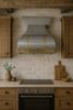 Wall-mount zinc metal range hood with brass straps in a farmhouse style kitchen