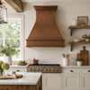 Hammered copper range hood in a bright farmhouse kitchen with white cabinetry and natural light