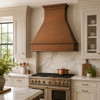 Hammered copper range hood in a traditional kitchen with detailed cabinetry and marble backsplash