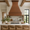 Island-mounted hammered copper range hood above a gas cooktop in a modern rustic kitchen