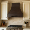 Strapless hammered copper hood in a transitional kitchen with pale cabinetry and stone backsplash