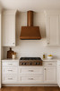 Old-World copper range hood with cylindrical chimney in a transitional kitchen with Shaker cabinets, quartz counters, and neutral tile