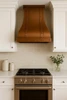 30-inch sweep copper range hood in a traditional kitchen with raised-panel cabinetry, natural stone backsplash, and warm wood finishes