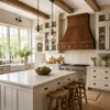 Round-hammered trapezoid copper range hood in bright farmhouse kitchen with painted cabinets, wood and stone