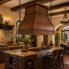 Spanish Colonial kitchen with hammered copper range hood, wide trim bands, kitchen island, copper sink, and hand-painted tile backsplash
