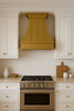 Transitional brass range hood wall mount in kitchen, smooth hand hammered brass canopy above cabinetry, stone backsplash and warm architectural finishes