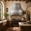 Spanish Colonial kitchen with a hammered zinc bell range hood, painted tile, wood beams, and terracotta floors