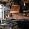 Double-beam copper range hood with vertical ribs on exposed brick wall in industrial loft kitchen