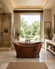 Mexican copper bathtub with rings in a bright luxury spa bathroom with natural stone, open space, and garden views