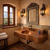 Copper bathroom sink with integrated hammered countertop in a Mexican hacienda bathroom furnished with Talavera tiles, terracotta floor, dark-stained wood vanity, wrought-iron mirror and bronze faucet