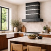 Dark zinc range hood with contrasting metal straps and rivets in organic kitchen with warm wood furniture and plaster walls