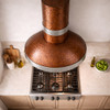 Hammered copper range hood with round chimney and zinc bands in kitchen island configuration