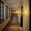 Traditional brass lantern chandeliers with scroll brackets in hotel corridor, repeated fixtures creating warm rhythm along hallway wall