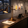 Industrial brass task lamp with counterweighted arm and heritage workshop on a gallery reception counter directs light to paperwork while reinforcing design identity