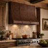Hand-Hammered Copper Range Hood with Adjustable Strap Layout in a rustic kitchen with reclaimed wood cabinetry and stone backsplash