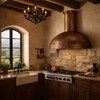 Hammered copper dome range hood with minimal apron in colonial hacienda kitchen with Saltillo tile floor