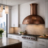 Hand hammered copper dome range hood with minimal apron in modern kitchen, warm patina canopy contrasting clean cabinetry and stone surfaces