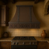 Spanish Colonial Revival copper range hood in Old European style kitchen, hammered canopy with warm patina above range and rustic stone details
