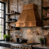 Hand-polished copper range hood with tapered design in industrial kitchen with brick wall