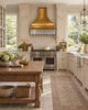 Brass range hood with zinc apron in an English Country kitchen with painted cupboards, warm oak, aged stone, and garden windows