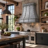 Industrial zinc range hood in bright loft kitchen with exposed brick, factory windows, reclaimed wood and black steel