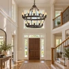 Two-tier iron chandelier in a sunlit two-story suburban foyer with an oak staircase and open upper landing