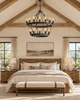 Two-tier iron chandelier in a bright vaulted primary bedroom with wood furniture, linen, and plaster walls