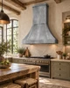Zinc bell range hood in a Rustic European kitchen with aged plaster, limestone and weathered oak