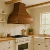 Handcrafted copper range hood with flared body and riveted bands in farmhouse kitchen, warm patina canopy above range with wood accents