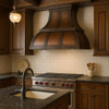 Copper range hood for gas stoves in traditional kitchen, hammered bell shaped canopy with decorative straps above classic cabinetry, stone backsplash and timeless architectural details