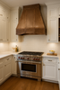 Wall mount pyramid shape copper hood for gas stove in transitional kitchen, warm patina canopy above range with balanced cabinetry