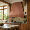 Hammered copper range hood in a bright Arts and Crafts kitchen with oak cabinetry, artisan tile, and natural light