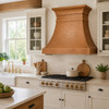 Honey patina copper range hood in bright farmhouse kitchen with cream cabinetry, stone counters