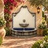 Arched stone wall fountain with talavera tiles in a hacienda garden with clay planters.