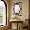 Wrought iron oval mirror in square scrollwork frame on foyer wall in a French style entry with console table