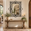 Rectangular ornate wrought iron mirror with scrollwork frame above a classic foyer console