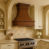 Copper bell range hood in a French Country kitchen with painted cabinetry, limestone, and warm wood accents