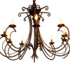 Wrought iron scroll arm chandelier with dark rust finish and candle-style bulbs glowing warmly
