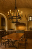 Hacienda style iron chandelier with candle lights in Tuscan kitchen with stone backsplash and wood beams