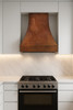 Copper vent hood with rooster motif in modern kitchen, hammered canopy with decorative apron above clean cabinetry and stone surfaces