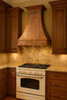 Copper range hood decorated with zinc straps and rivets in traditional kitchen, hammered copper canopy above classic cabinetry with contrasting metal accents