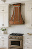 Copper range hood decorated with zinc straps and rivets in transitional kitchen, warm hammered copper canopy above balanced cabinetry and stone surfaces