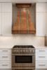 Copper range hood decorated with zinc straps and rivets in modern kitchen, warm copper focal point contrasting white cabinetry and minimalist surfaces
