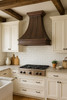 Copper range hood in farmhouse kitchen, handcrafted metal canopy above shiplap walls, natural wood cabinetry and rustic accents