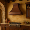 Old European copper range hood with decorative scroll motif in Tuscan kitchen, hammered copper canopy with warm patina finish