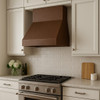Simple under cabinet copper range hood in transitional kitchen setting, compact hammered canopy with warm patina above balanced cabinetry