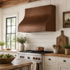 Hammered box copper range hood in rustic farmhouse kitchen with white shiplap, wood beams, and warm patina